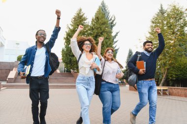 Group of diverse college students walking and raising fists in air, celebrating academic success and graduation on campus