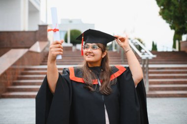 Indian woman graduate celebrating her diploma and academic achievement, standing outdoors near a university building