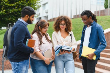 Group of diverse university students collaborating, discussing, and learning outside on campus, holding books and looking at notes