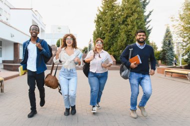 Diverse group of happy young students walking and smiling on a university campus, holding books and backpacks