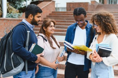 Group of diverse university students collaborating and learning together near campus building, holding books
