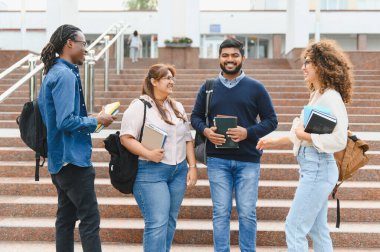 Diverse group of college students standing on university steps, holding books and backpacks, engaging in conversation
