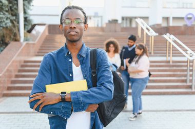 African american student carrying backpack and book on university campus, other students in background, focusing on education and learning
