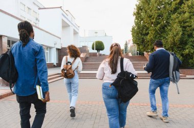Group of diverse postgraduate students arriving for classes, carrying backpacks and books on a college campus