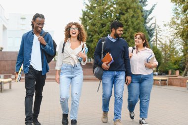 Diverse group of college students walking together on campus, smiling, and carrying books. Representing education, friendship, and diversity
