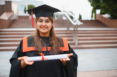 Indian woman graduating university, wearing academic gown and cap, holding her diploma with a proud smile