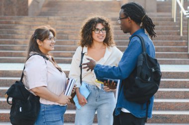 Diverse students standing on campus stairs, carrying books and backpacks, engaging in an animated discussion about education