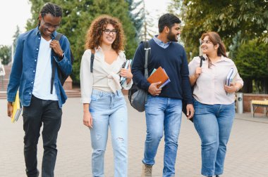 Group of happy young adults from different ethnicities and cultures walking, talking, and smiling outdoors on a university campus