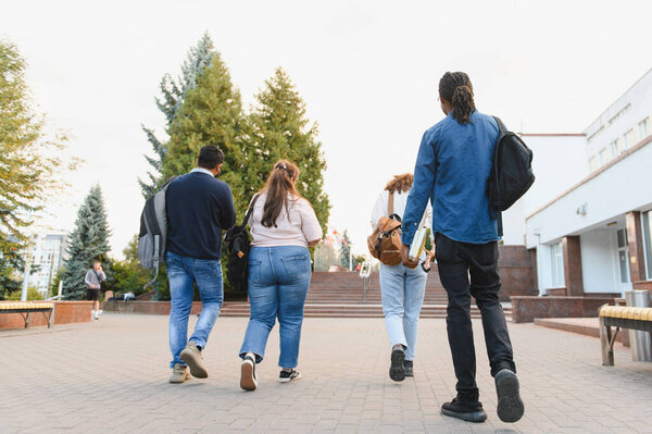 Group of multiethnic high school or college students with backpacks and books walking across campus on a sunny day