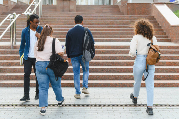 Diverse group of young students with backpacks ascending granite stairs, heading towards a university building