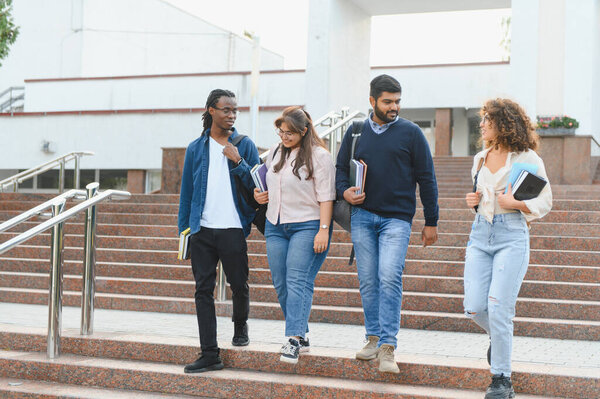 Group of diverse university students carrying books and backpacks, walking down granite stairs on campus