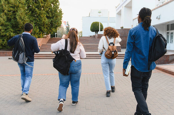 Group of diverse college students walking away on a university campus pavement, carrying backpacks and books