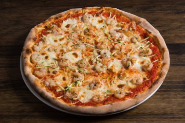 Ev yapımı bir Cajun karides pizzası fırından yeni çıkmış kahverengi bir parşömen kağıdının üzerinde duruyor.