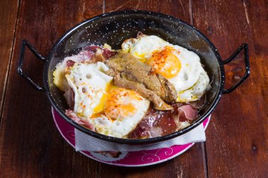 Jambonlu, patatesli ve soslu huevos rotos.