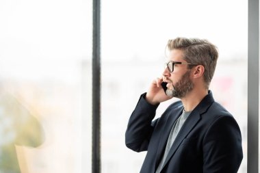 Ofiste dikilirken ve telefonla konuşurken kendine güvenen iş adamının takım elbise giydiği yakın plan..