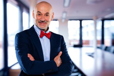 Ofiste duran kendinden emin erkek CEO 'nun portresi. Olgun yönetici takım elbise ve papyon takıyor. İş adamı kameraya bakıp gülümserken kollarını kavuşturuyor..