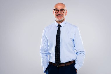 Tecrit edilmiş arka planda duran kendine güvenen erkek CEO portresi. Olgun yönetici gözlük takıyor. Açık gri arka plana gülümsüyor. Boşluğu kopyala.