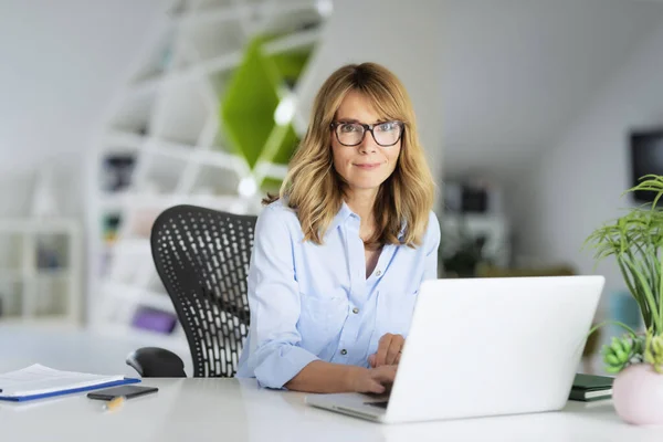 自信的女商人坐在办公室里 在笔记本电脑上工作 迷人的女性 穿着眼镜和衬衫 看着相机 微笑着 — 图库照片