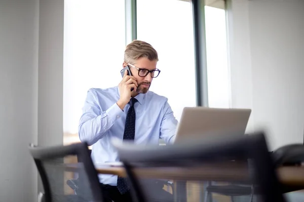 ビジネスの専門家は ラップトップでテーブルに座って 携帯電話で話して考えています シャツを着てネクタイをしているビジネスマン — ストック写真