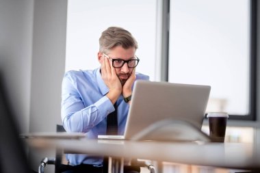 Ofiste çalışıp dizüstü bilgisayar kullanan orta yaşlı bir işadamı. Profesyonel adam endişeli görünüyor..