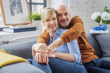Shot of married couple embracing on sofa. Happy woman and man wearing casual clothes while relaxing at home.
