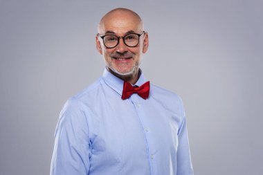 Close-up of mid aged man wearing shirt and bow tie and standing at isolated grey background. Copy space.