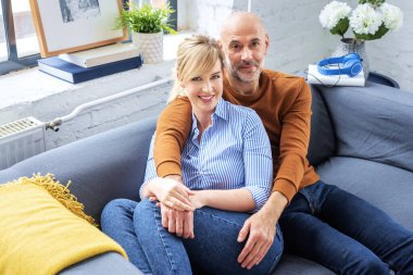 Shot of married couple embracing on sofa. Happy woman and man wearing casual clothes while relaxing at home.