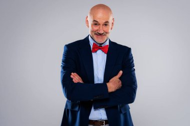 Studio portrait of mid aged man wearing bow tie and blazer while standing at isolated grey background. Copy space.