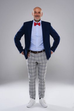 Full length studio shot of smiling man wearing bow tie and checked trousers while standing at isolated grey background. Copy space.