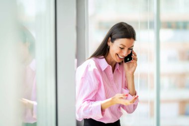 Smiling businesswoman standing at the office while using smartphone.. Professional female having a business call. 