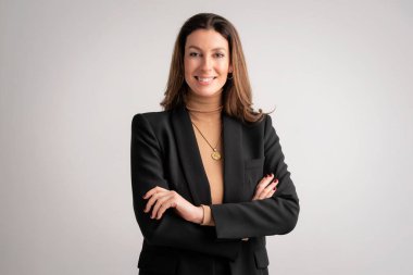 Close-up of an attractive mid aged woman smiling and looking at camera. Brunette haired female wearing black blazer and standing at isolated background. Copy space. 