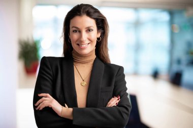 Close-up of an executive professional woman smiling and looking at camera. Brunette haired businesswoman wearing blazer while standing at the office. Copy space. 