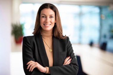 Close-up of an executive professional woman smiling and looking at camera. Brunette haired businesswoman wearing blazer while standing at the office. Copy space. 