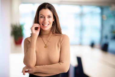 Close-up of an attractive middle aged female cheerful smiling and looking at camera. Brunette haired businesswoman wearing sweater while standing at the office. Copy space. 