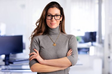 Portrait of attractive middle aged business woman wearing eyewear and turtleneck sweater while standing inside. 