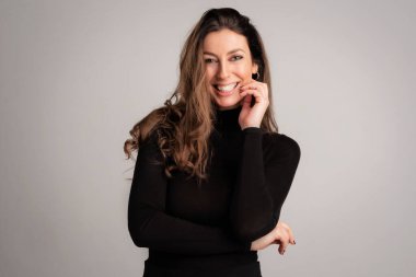 Close-up of an attractive middle aged woman with toothy smile wearing turtleneck sweater while standing at isolated grey background. Copy space. Studio shot.