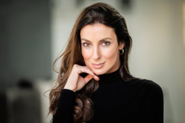 Close-up portrait of an attractive brunette haired woman looking at camera and smiling. Headshot of brunette haired female wearing turtleneck sweater.