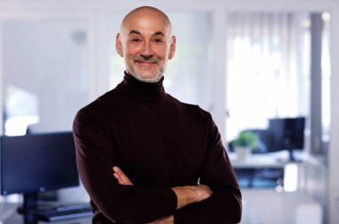 Gri arka planda duran kendine güvenen bir adamın yakın çekimi. Boğazlı kazak giyen gülümseyen işadamı kameraya bakıyor.. 