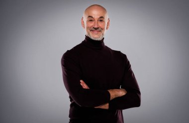 Gri arka planda duran kendine güvenen bir adamın yakın çekim portresi. Gülümseyen erkek kameraya bakıyor ve balıkçı yaka kazak giyiyor. Boşluğu kopyala. 