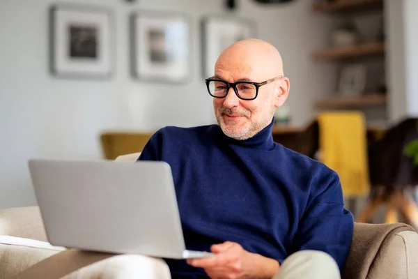 Orta Yaşlı Adamı Evdeki Koltukta Oturuyor Için Dizüstü Bilgisayar Kullanıyor — Stok fotoğraf