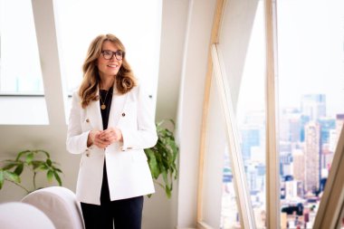 Çekici orta yaşlı bir kadının portre resmi. Neşeli bir şekilde gülümseyen ve pencereden dışarı bakan.. 