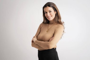 Close-up of an attractive mid aged woman smiling and looking at camera. Brunette haired female wearing turtleneck sweater while standing at isolated background. Copy space. 