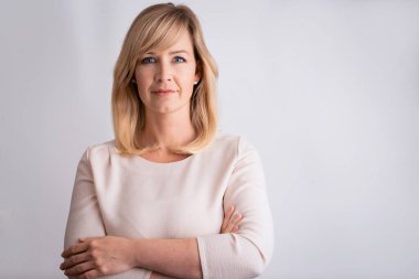 Yalıtılmış arka planda dikilirken gündelik kıyafetler giyen orta yaşlı sarışın bir kadının stüdyo portresi. Boşluğu kopyala.