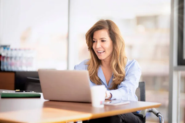 一名中年职业女性穿着衬衫 在一间现代化的办公室工作时使用笔记本电脑 坎迪拍摄的照片 迷人的女商人坐在办公桌前 开电视电话会议 — 图库照片