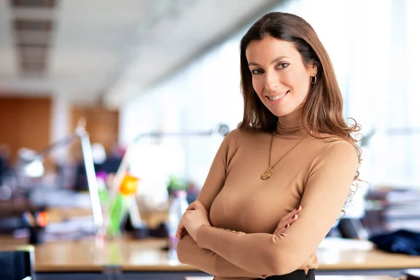 Shot of an attractive mid aged woman cheerful smiling and looking at camera. Brunette haired female wearing turtleneck sweater and standing in the office. Copy space.