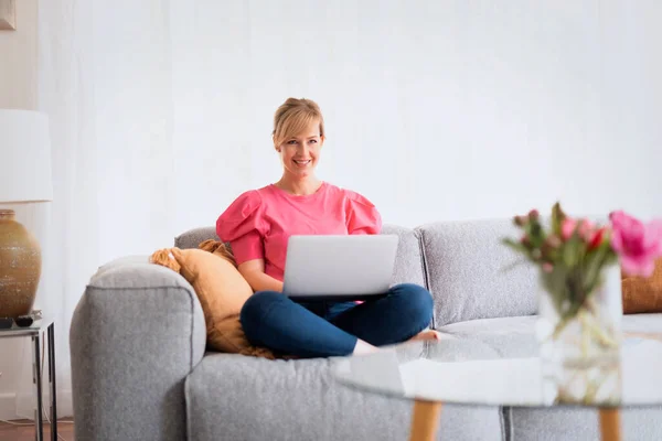 Een Glimlachende Blonde Vrouw Die Thuis Bank Zit Laptop Gebruikt — Stockfoto