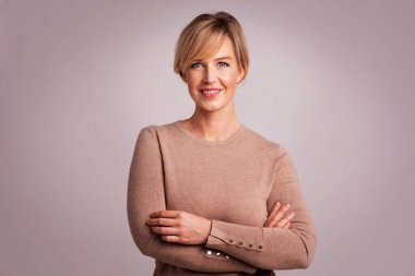 Kolları çaprazlanmış, izole edilmiş, çekici, sarışın bir kadın. Süveter giyip kameraya bakan orta yaşlı bir kadın. Boşluğu kopyala. 