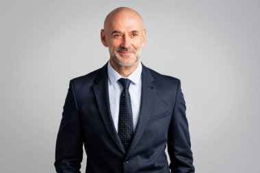 Kel kafalı, kendinden emin bir iş adamının portresi. Takım elbiseli, kravatlı ve beyaz arka plandaki kameraya bakan kıdemli profesyonel bir adam..