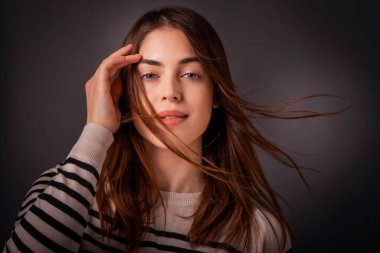 İzole edilmiş arka planda duran gülümseyen kadın portresi. Kendine güvenen genç bir bayanın kumral saçları var. Siyah arka planda çizgili süveter giyiyor. Boşluğu kopyala. 