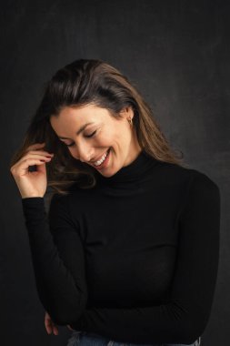 Çekici, orta yaşlı, dişlek, balıkçı yaka kazak giyen ve arka planda yalnız duran bir kadının stüdyo portresi. Boşluğu kopyala.